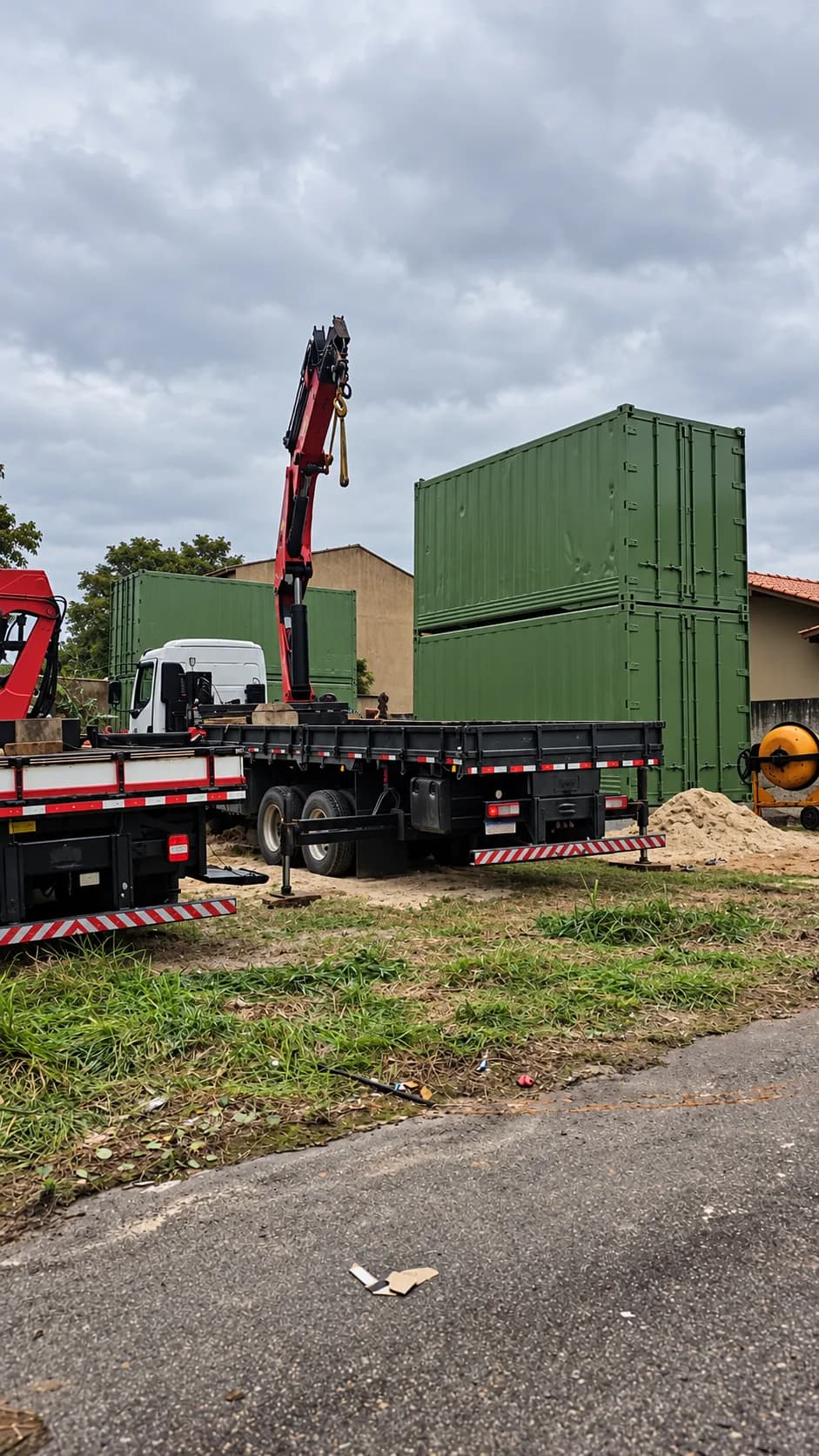 Containers verdes empilhados no terreno, recém-entregues por caminhão munck, antes da transformação.